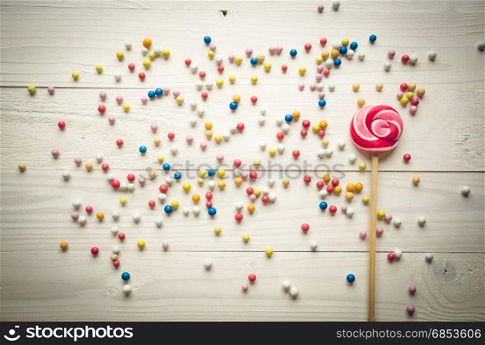 Colorful little candies and big lollipop on white wooden background