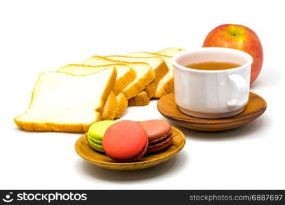Colorful macarons on wooden plate, sliced bread, red apple and a cup of hot tea on white background