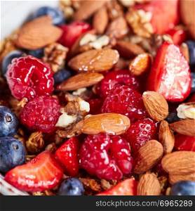 Colorful mix of berries, nuts, oatmeal, granola and honey close-up. Ingredients for dietary nutrition. Healthy vegetarian food.. Natural organic raspberry, strawberry, blueberry, nuts, oat flax and honey are a healthy breakfast background.