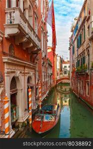Colorful narrow lateral canal and pedestrian bridge in Venice with docked boats, Italy