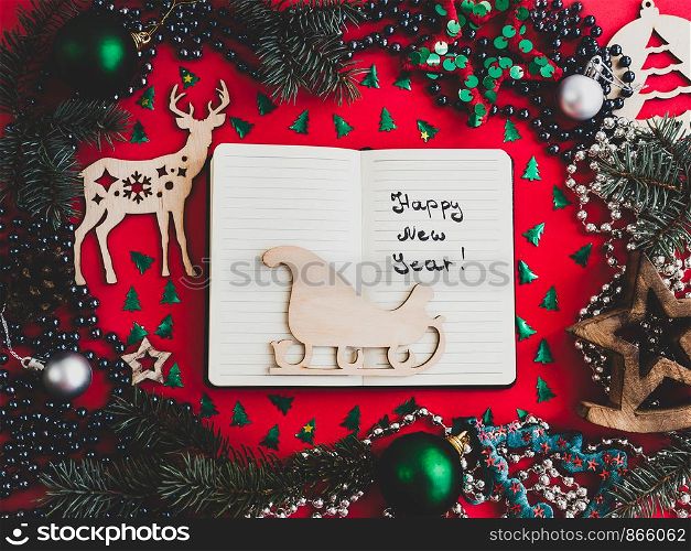 Colorful New Year and Christmas decorations, silver beads, branches of the Christmas tree, drawing in a notebook on a red surface. Top view, close-up, flat lay. Greeting card. Colorful New Year and Christmas decorations, . Greeting card