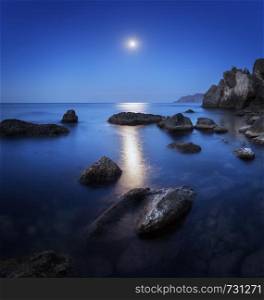 Colorful night landscape with full moon, lunar path and rocks in summer. Mountain landscape at the sea