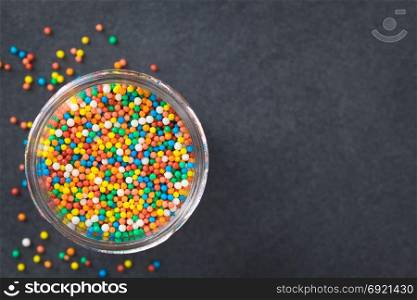 Colorful nonpareils sugar sprinkles in glass jar, photographed overhead on slate (Selective Focus, Focus on the nonpareils in the jar). Colorful Nonpareils Sugar Sprinkles