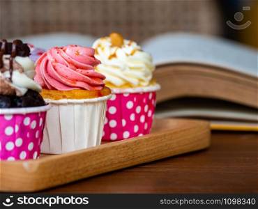 Colorful of homemade cupcake on wooden tray on and open book on wooden table. Concept of lifestyle and relax.