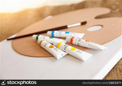 Colorful oil paints in tubes and paintbrush lying on wooden pallet