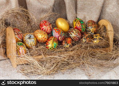 Colorful painted easter egg on hay in wooden shelf with sack background