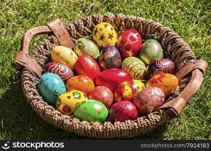 Colorful painted Easter eggs in basket on green grass background