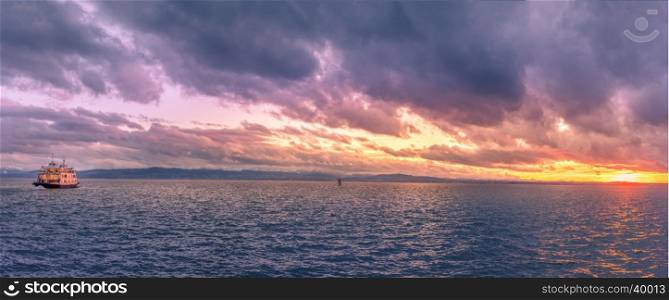 Colorful panorama with the lake Bodensee, in Friedrichshafen, Germany, at sunset, after a storm, while a boat sails on its water.