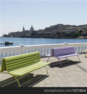 Colorful park benches on the embankment of Valletta. Promenade on the background of the bay in Malta