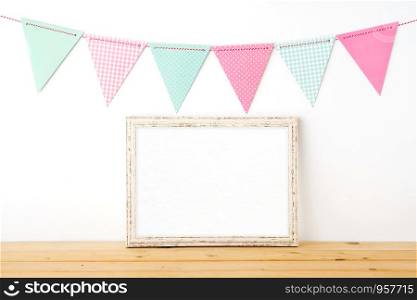 Colorful party flags hanging over blank white vintage wooden frame on wood table background, birthday, anniversary, celebrate event, festival background