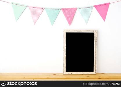 Colorful party flags hanging over blank white vintage wooden frame on wood table background, birthday, anniversary, celebrate event, festival background