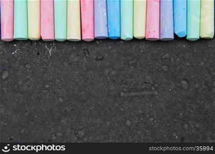 Colorful pastel sidewalk chalk on dark asphalt background. Top view