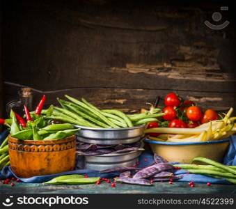 Colorful pea and bean pods in bowls on rustic kitchen table at wooden background, top view. Healthy vegetarian food concept