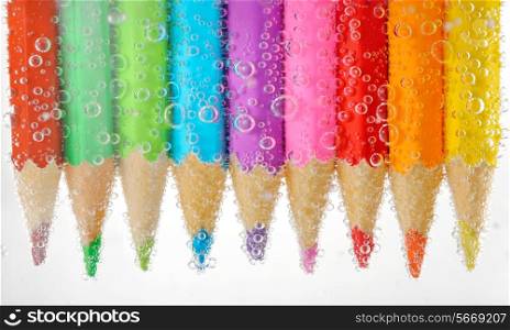 Colorful pencils in water with bubbles, isolated on white