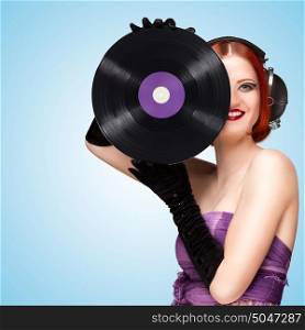 Colorful photo of a beautiful sexy girl wearing big vintage music headphones and holding a purple LP microgroove vinyl record in her hands on blue background.