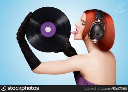 Colorful photo of a seductive girl, wearing huge vintage music headphones and licking a purple LP microgroove vinyl record on blue background.
