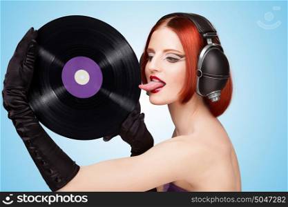 Colorful photo of a sexy girl, wearing huge vintage music headphones and licking a purple LP microgroove vinyl record on blue background.