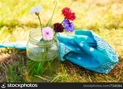 Colorful picked cornflowers in glass jar standing outdoor in the garden