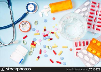 Colorful pills with glass of clear water over blue background. Medical pharmacy concept. Pile of pills