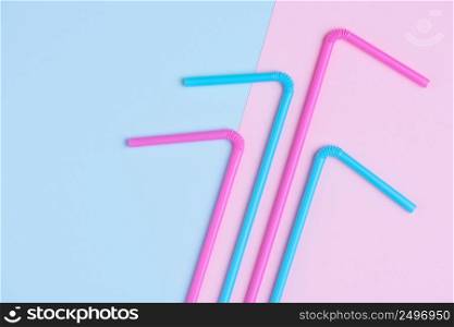 Colorful plastic drinking coocktail straws on pink and blue trendy pastel background