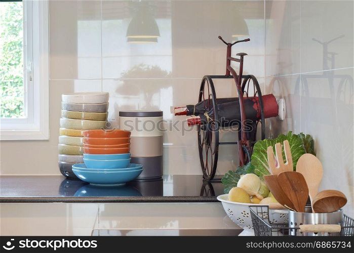 Colorful plates and bowls and wine bottles on black granite top in the kitchen