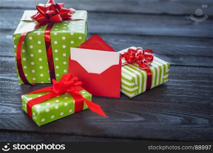 Colorful presents, wrapped in paper and tied with red ribbon and bows, with an opened red letter leaned against them, on vintage background.