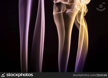 Colorful purple and yellow smoke of incence sticks isolated at black background. Colorful smoke of incence stick isolated at black background