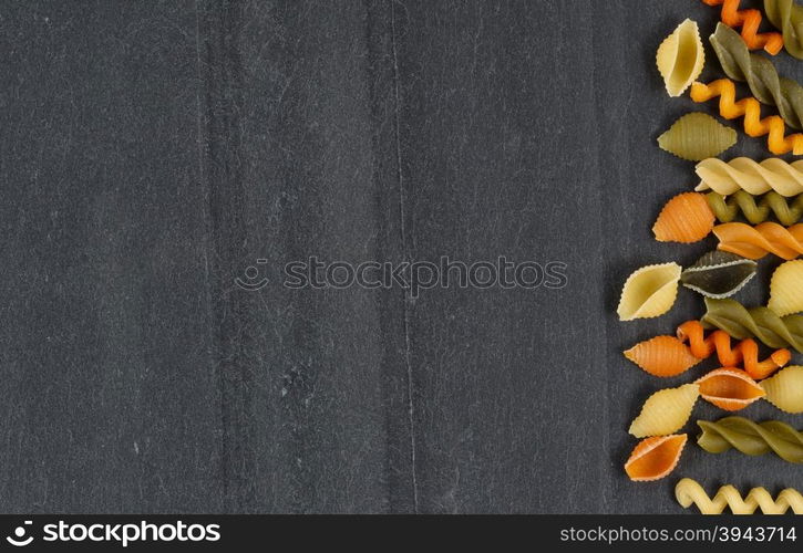 Colorful raw pasta on natural black slate stone. Horizontal layout.