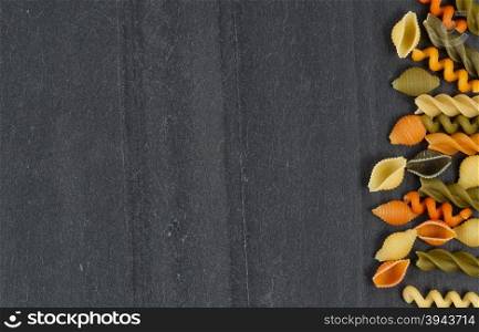Colorful raw pasta on natural black slate stone. Horizontal layout.