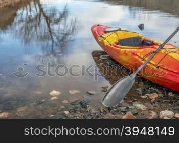 colorful river kayak with a paddle on rocky lake shore with a tree reflection - recreation concept