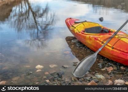 colorful river kayak with a paddle on rocky lake shore with a tree reflection - recreation concept