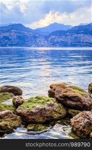 Colorful rocks and reflections in the lake Lago di Garda. Clear water, mountains and sky.