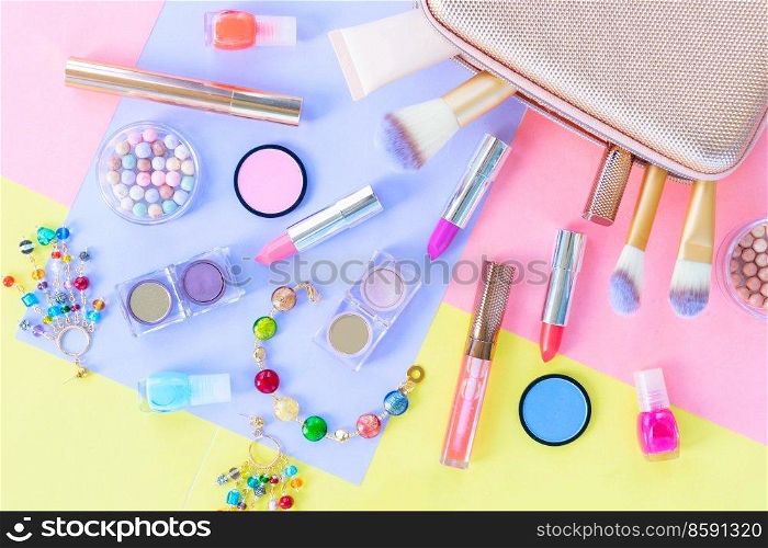 Colorful scattered make up products with golden pursue close up on plain color block background. Colorful make up flat lay scene