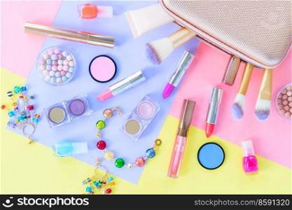 Colorful scattered make up products with golden pursue close up on plain color block background. Colorful make up flat lay scene