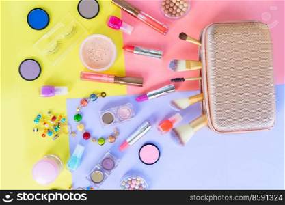 Colorful scattered make up products with golden pursue on plain color block background. Colorful make up flat lay scene