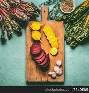 Colorful sliced beetroots with greens ingredients on kitchen table with cutting board, top view. Healthy vegetarian eating and cooking