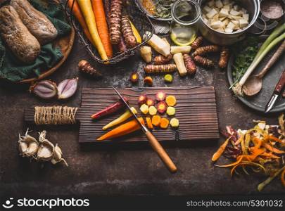 Colorful sliced carrots with knife on wooden cutting board on rustic kitchen table background with root vegetables ingredients for tasty vegetarian cooking, top view. Healthy food and eating