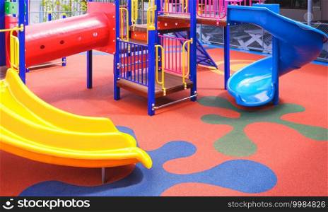 Colorful slides with playground climbing equipment on rubber floor in outdoors playground area at kindergarten