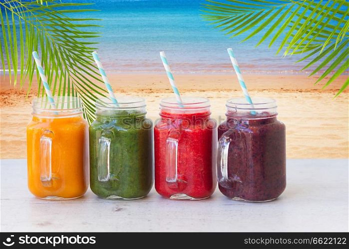 Colorful smoothy drinks in glass jars on white table by beach. Fresh smoothy drink