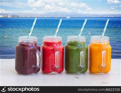 Colorful smoothy drinks in glass jars on white table by seaside. Fresh smoothy drink