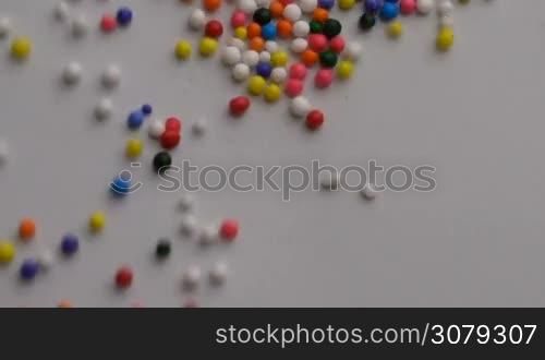 Colorful sprinkles sugar candy moving on white surface background