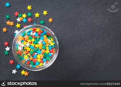 Colorful star shaped sugar sprinkles in glass jar, photographed overhead on slate (Selective Focus, Focus on the sprinkles in the jar). Colorful Star Shaped Sugar Sprinkles