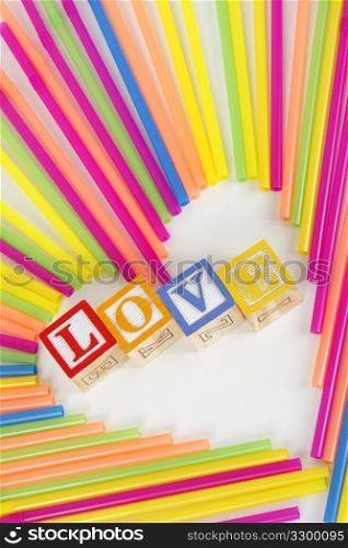 Colorful Straws make a heart shape and childrens bloks spell the word Love.
