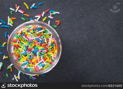 Colorful sugar sprinkles in glass jar, photographed overhead on slate (Selective Focus, Focus on the sprinkles in the jar). Colorful Sugar Sprinkles
