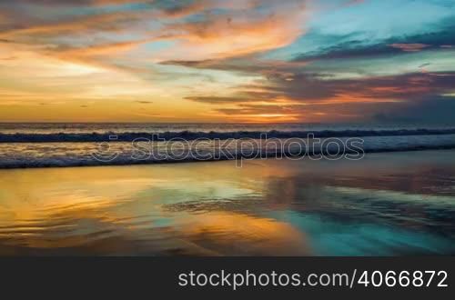 Colorful sunset at ocean with reflections on sand