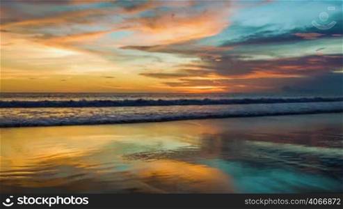Colorful sunset at ocean with reflections on sand