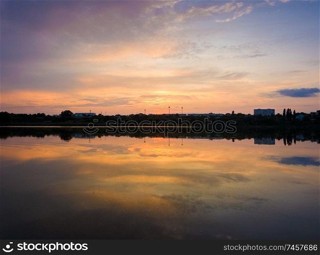 Colorful sunset clouds symmetric reflected on the lake surface. Idyllic summer evening, natural scene near a countryside pond with calm water.