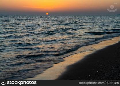 colorful sunset on the Mediterranean Sea in Greece with calm ocean water and dark sand beach in the foreground