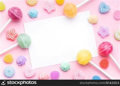 Colorful sweet lollipops and candies and empty greeting card  over pink background.  Flat lay, top view