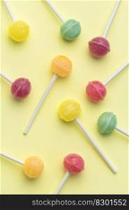 Colorful sweet lollipops over yellow background.  Flat lay, top view